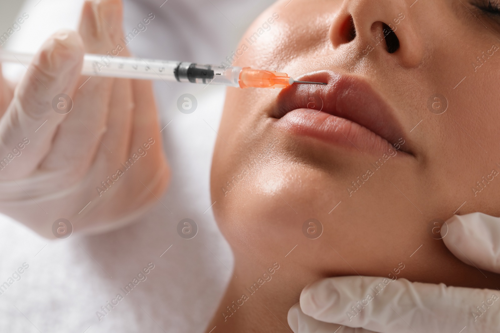 Photo of Doctor giving lips injection to young woman in clinic, closeup. Cosmetic surgery