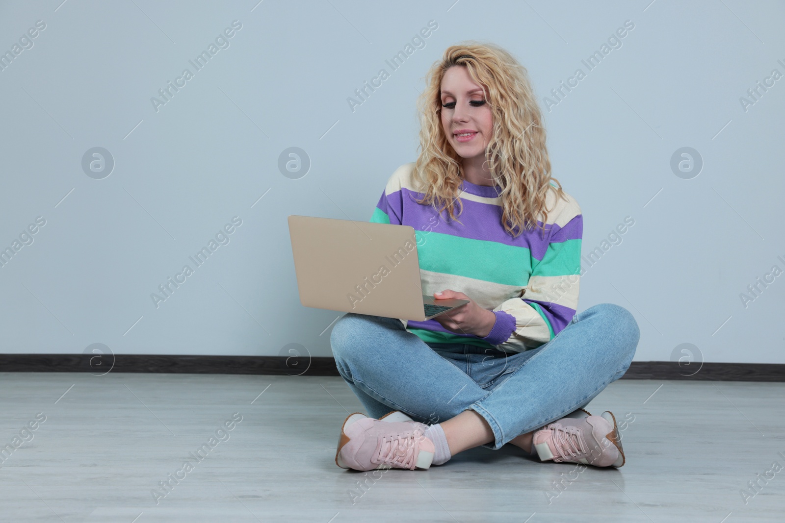 Photo of Beautiful young woman with laptop sitting on floor near grey wall. Space for text