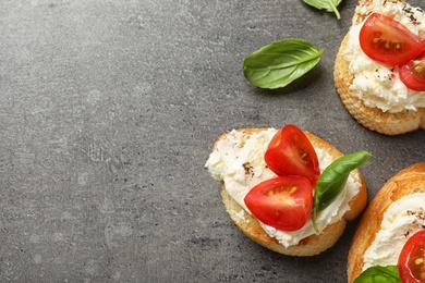 Pieces of baguette with tasty cream cheese and tomatoes on gray table, flat lay. Space for text