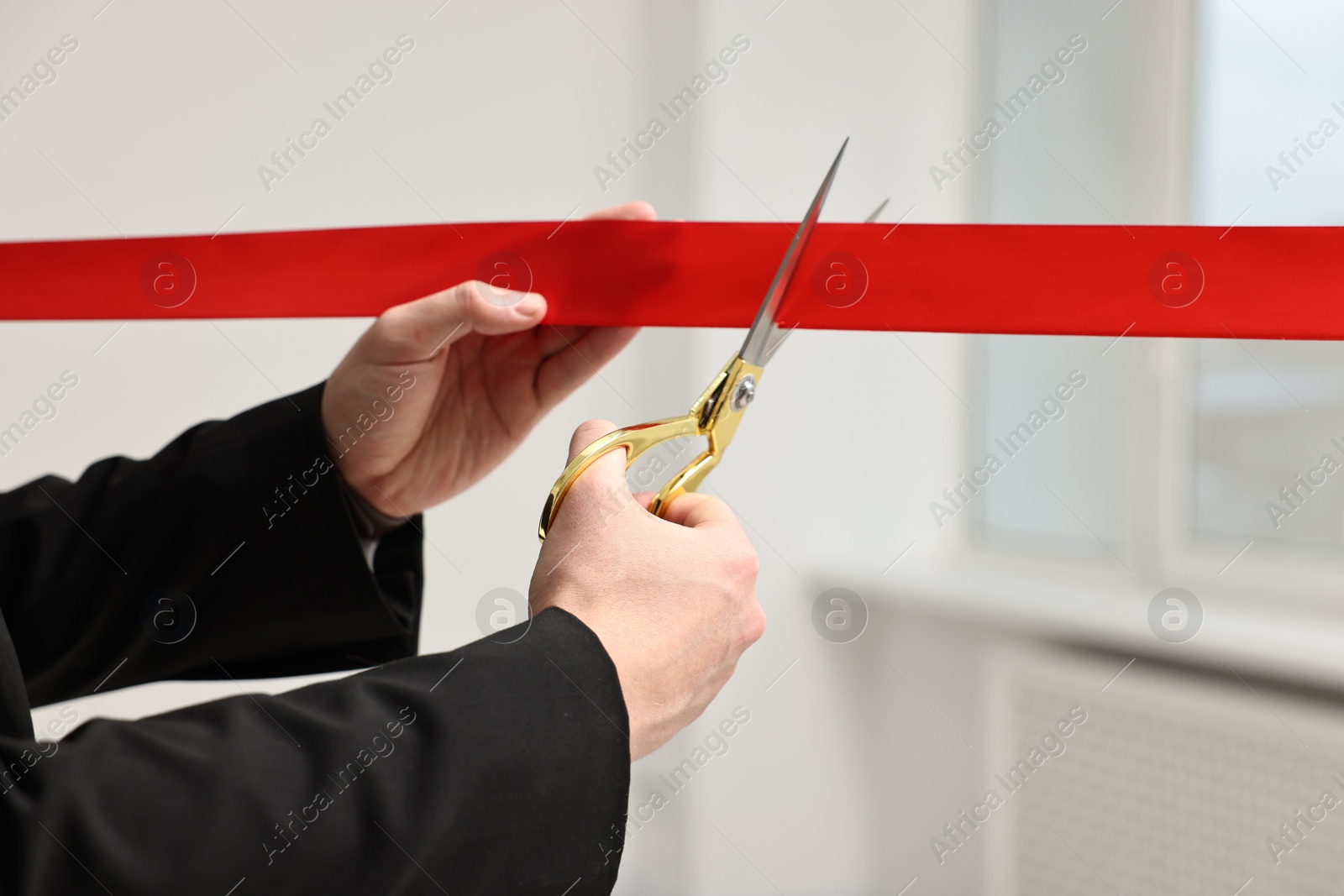 Photo of Woman cutting red ribbon with scissors indoors, closeup