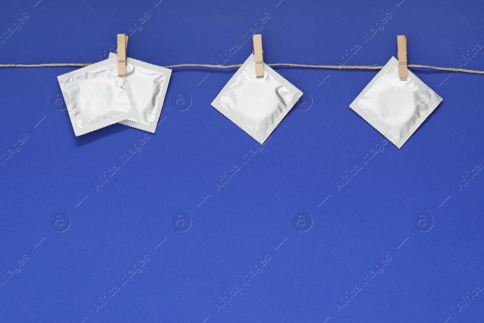 Photo of Clothesline with packaged condoms on blue background, space for text. Safe sex