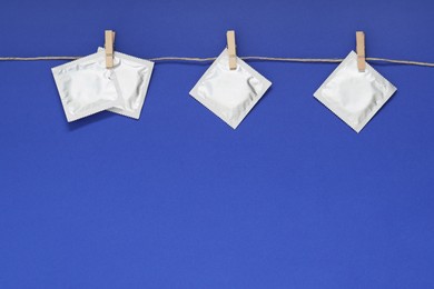 Photo of Clothesline with packaged condoms on blue background, space for text. Safe sex