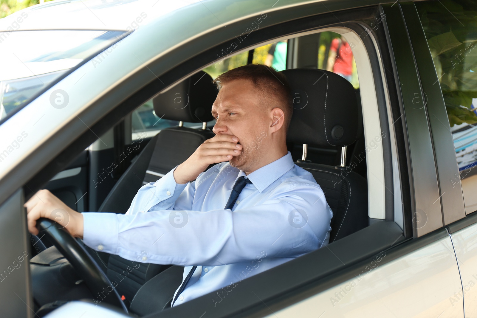 Photo of Tired young man yawning in his car