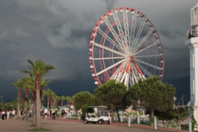 Blurred view of large Ferris wheel in park under rainy clouds