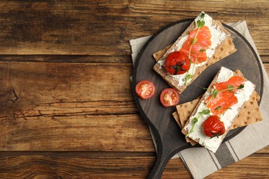 Photo of Fresh rye crispbreads with salmon, cream cheese and tomatoes on wooden table, top view. Space for text