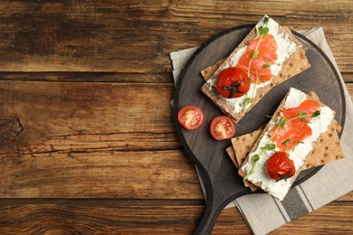 Fresh rye crispbreads with salmon, cream cheese and tomatoes on wooden table, top view. Space for text