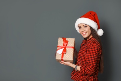 Young woman with Christmas gift on grey background