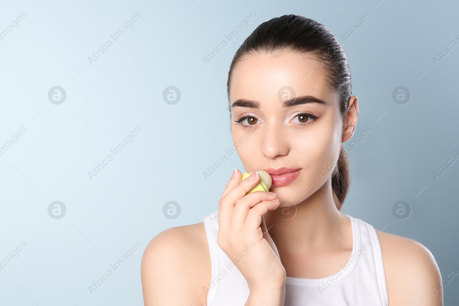 Photo of Young woman applying balm on her lips against color background