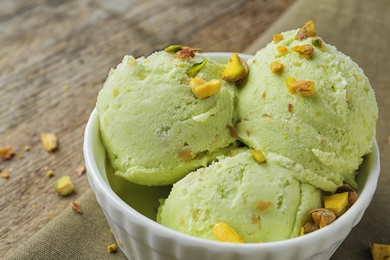 Photo of Delicious green ice cream served in ceramic bowl on wooden table, closeup