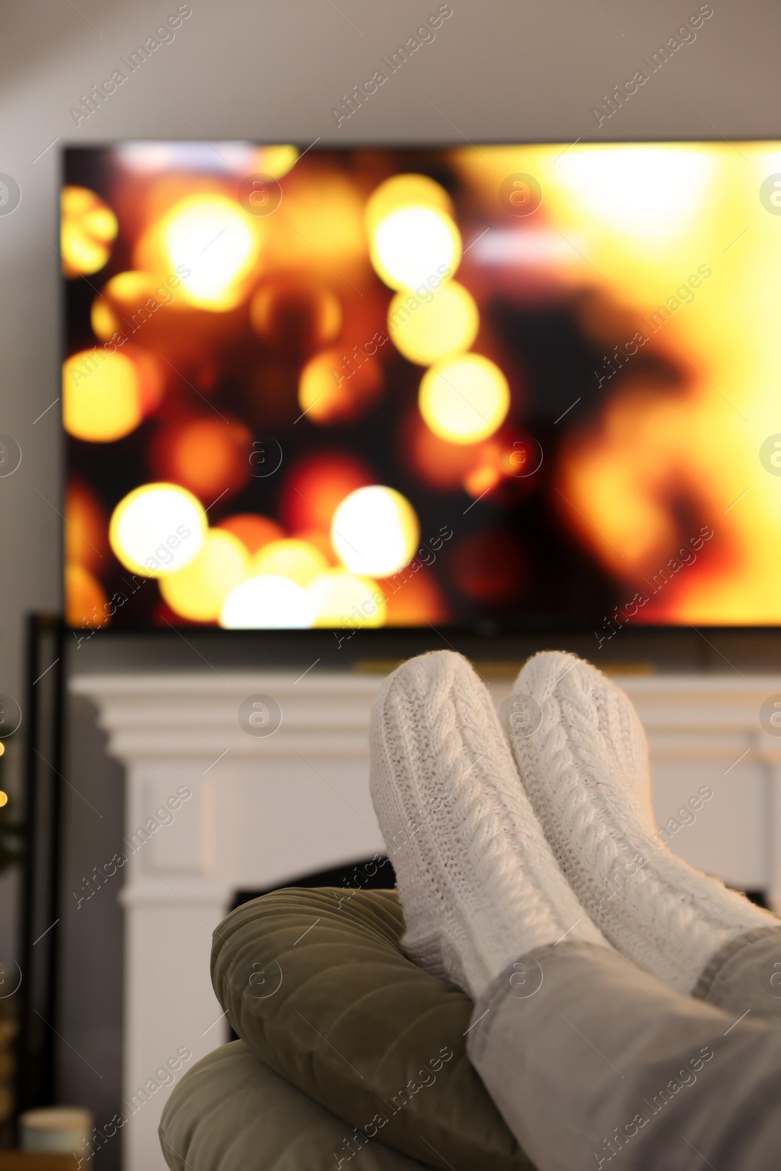 Photo of Woman wearing knitted socks in room decorated for Christmas, closeup