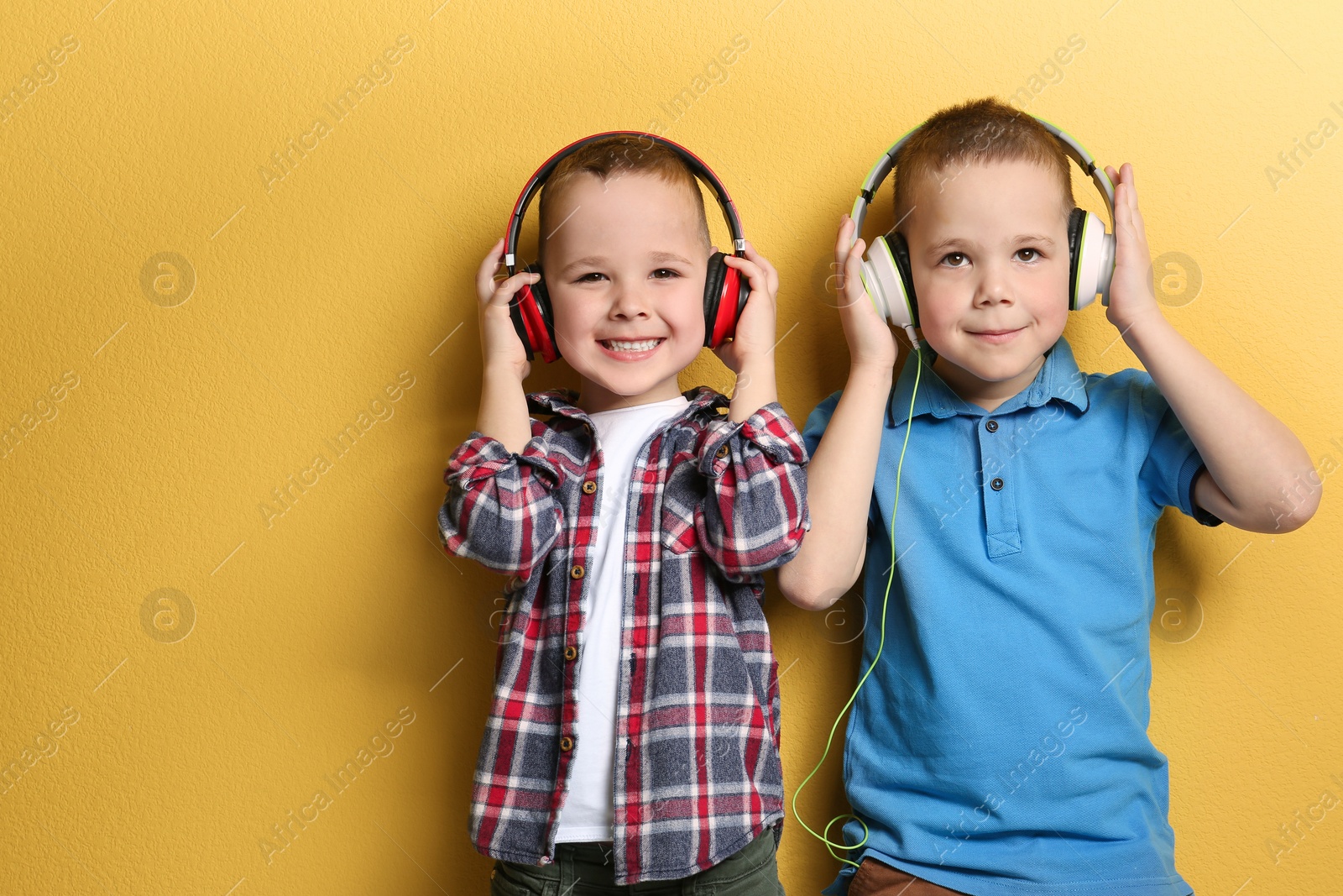 Photo of Portrait of cute twin brothers with headphones on color background