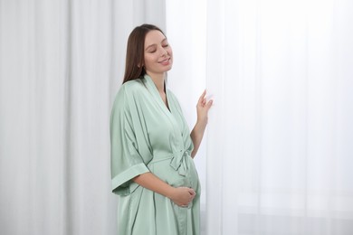 Photo of Beautiful pregnant woman in green dressing gown near window indoors