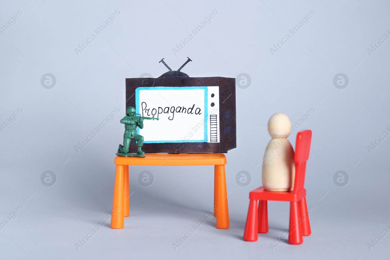 Photo of Hybrid warfare concept. Human figure watching TV propaganda at gunpoint by toy soldier on light grey background