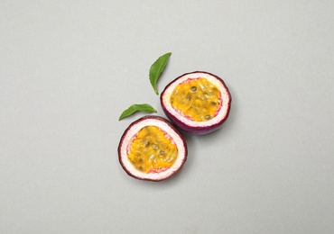 Halves of fresh ripe passion fruit (maracuya) and leaves on grey background, flat lay