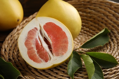 Photo of Fresh cut and whole pomelo fruits with leaves on wicker mat, closeup