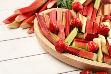 Photo of Cut fresh rhubarb stalks and strawberries on white wooden table, closeup. Space for text