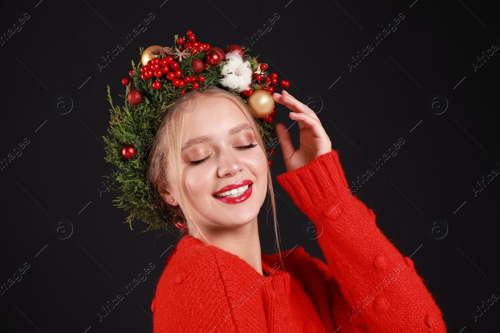 Photo of Beautiful young woman wearing Christmas wreath on black background