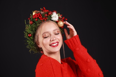 Photo of Beautiful young woman wearing Christmas wreath on black background