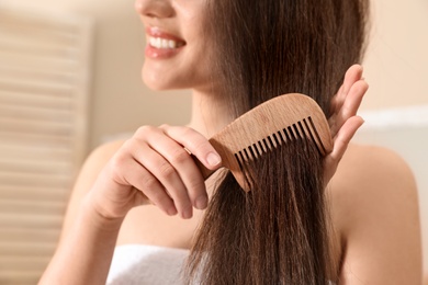 Photo of Beautiful young woman with hair comb in bathroom, closeup