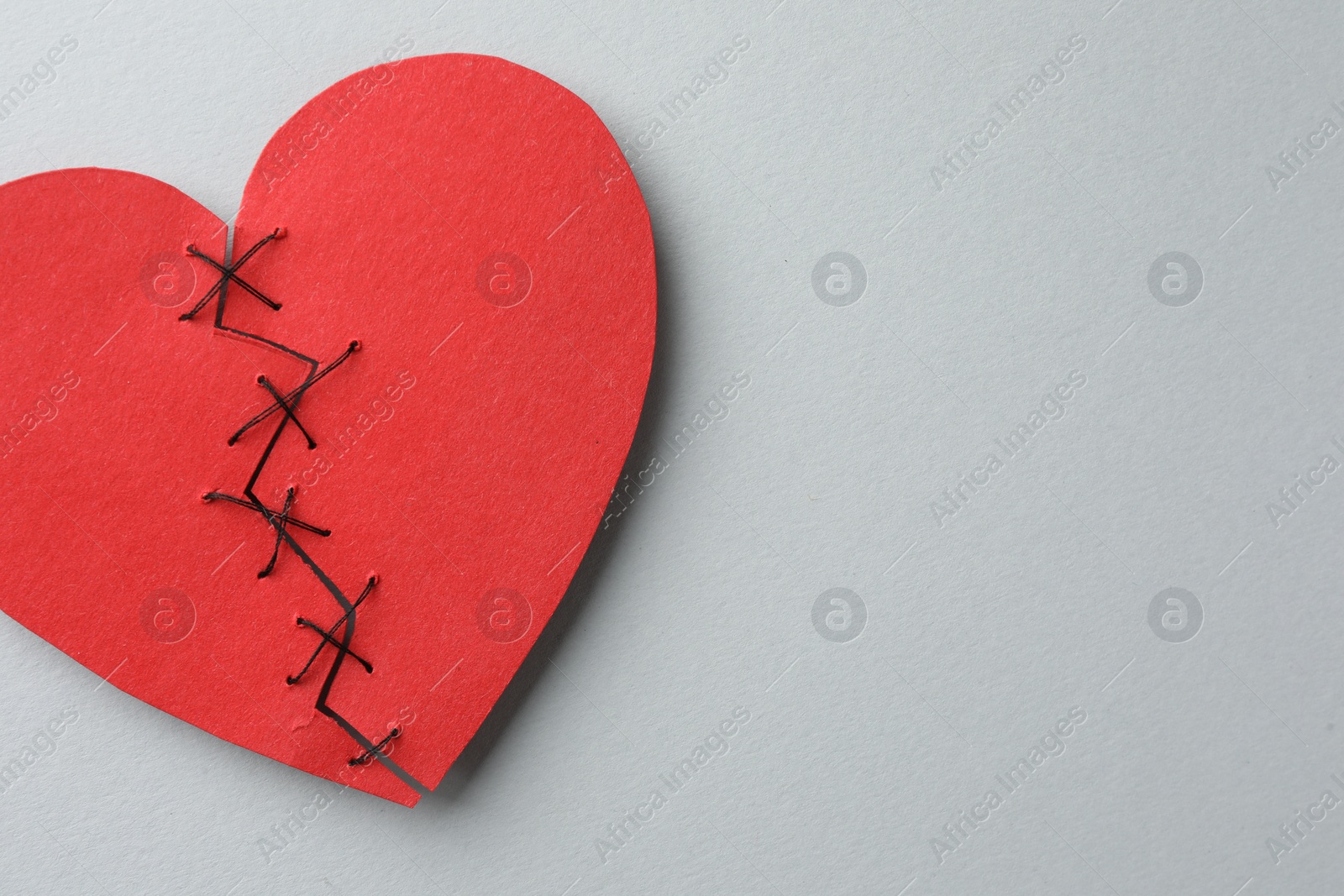 Photo of Broken heart. Torn red paper heart sewed with thread on light grey background, top view. Space for text