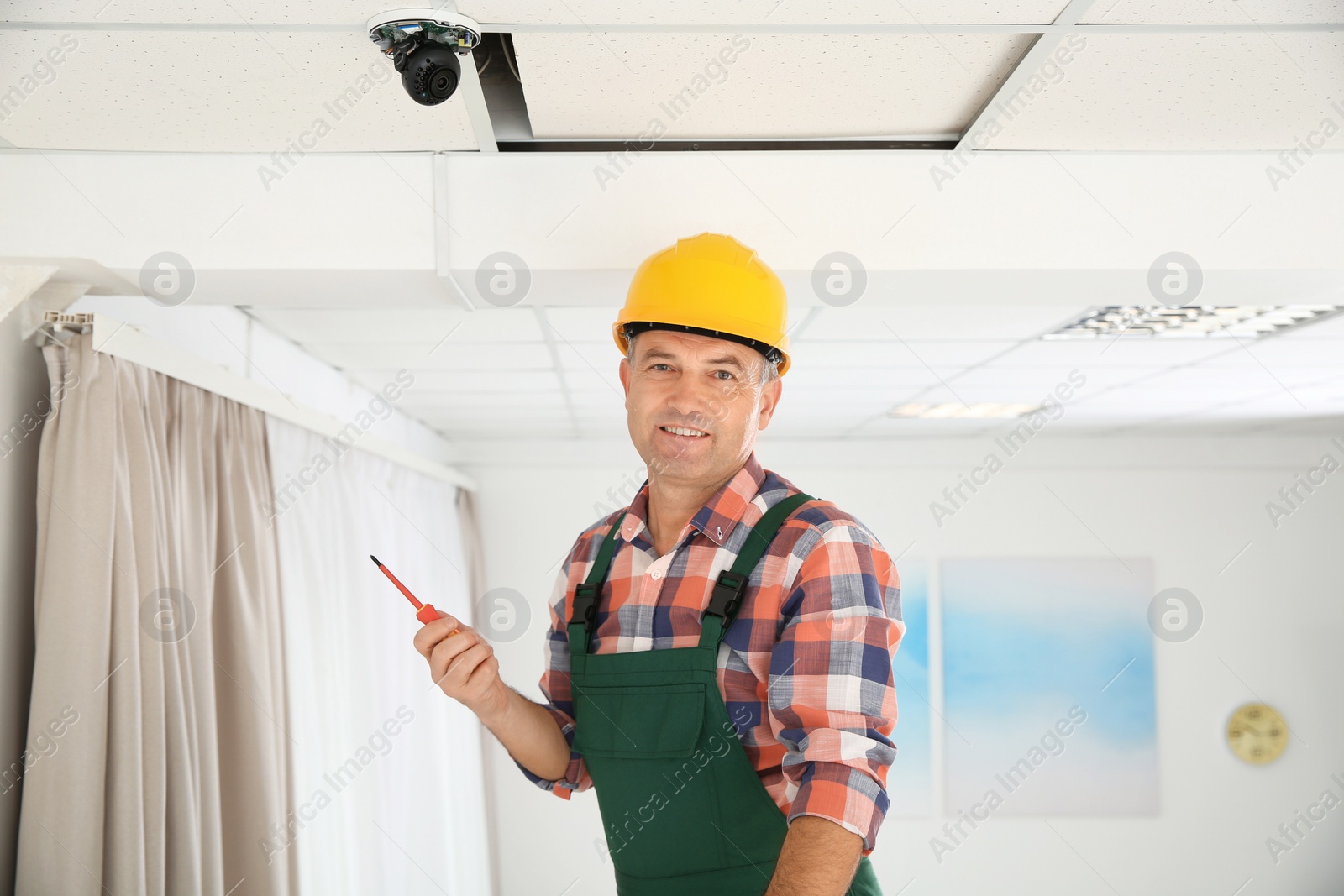 Photo of Electrician with screwdriver repairing CCTV camera indoors