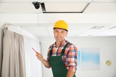 Electrician with screwdriver repairing CCTV camera indoors