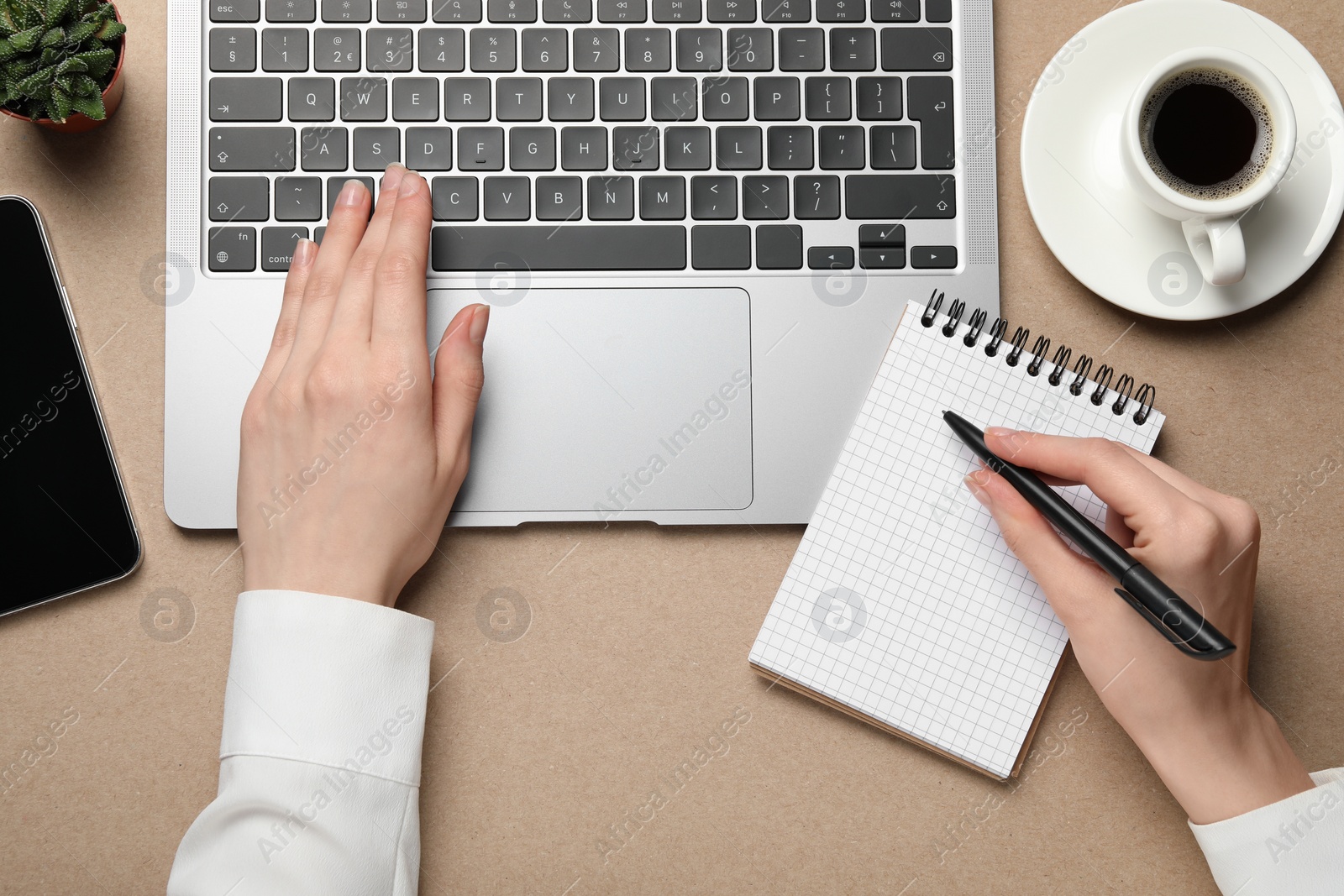 Photo of Woman using laptop and writing notes at beige table, top view