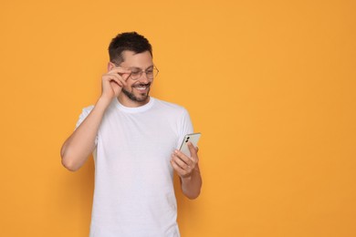 Photo of Happy man with smartphone on orange background. Space for text