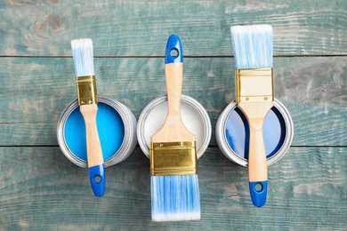 Open cans with paint and brushes on blue wooden table, flat lay