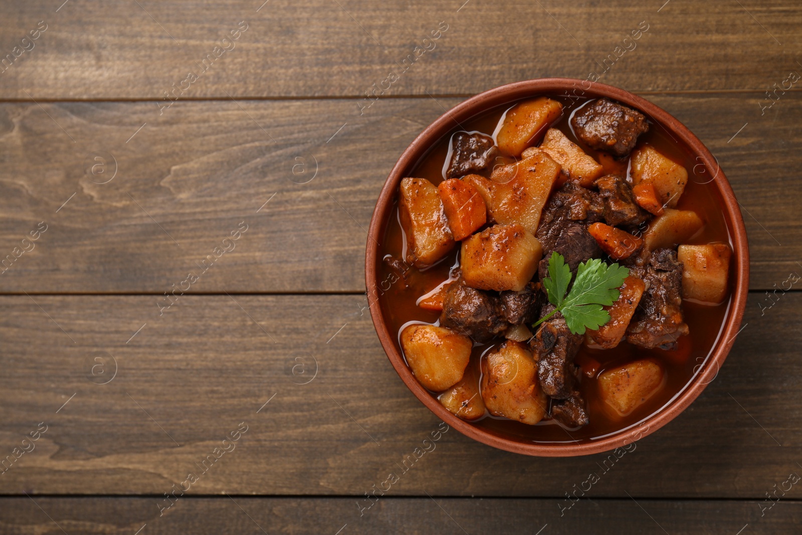 Photo of Delicious beef stew with carrots, parsley and potatoes on wooden table, top view. Space for text