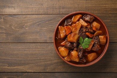 Photo of Delicious beef stew with carrots, parsley and potatoes on wooden table, top view. Space for text