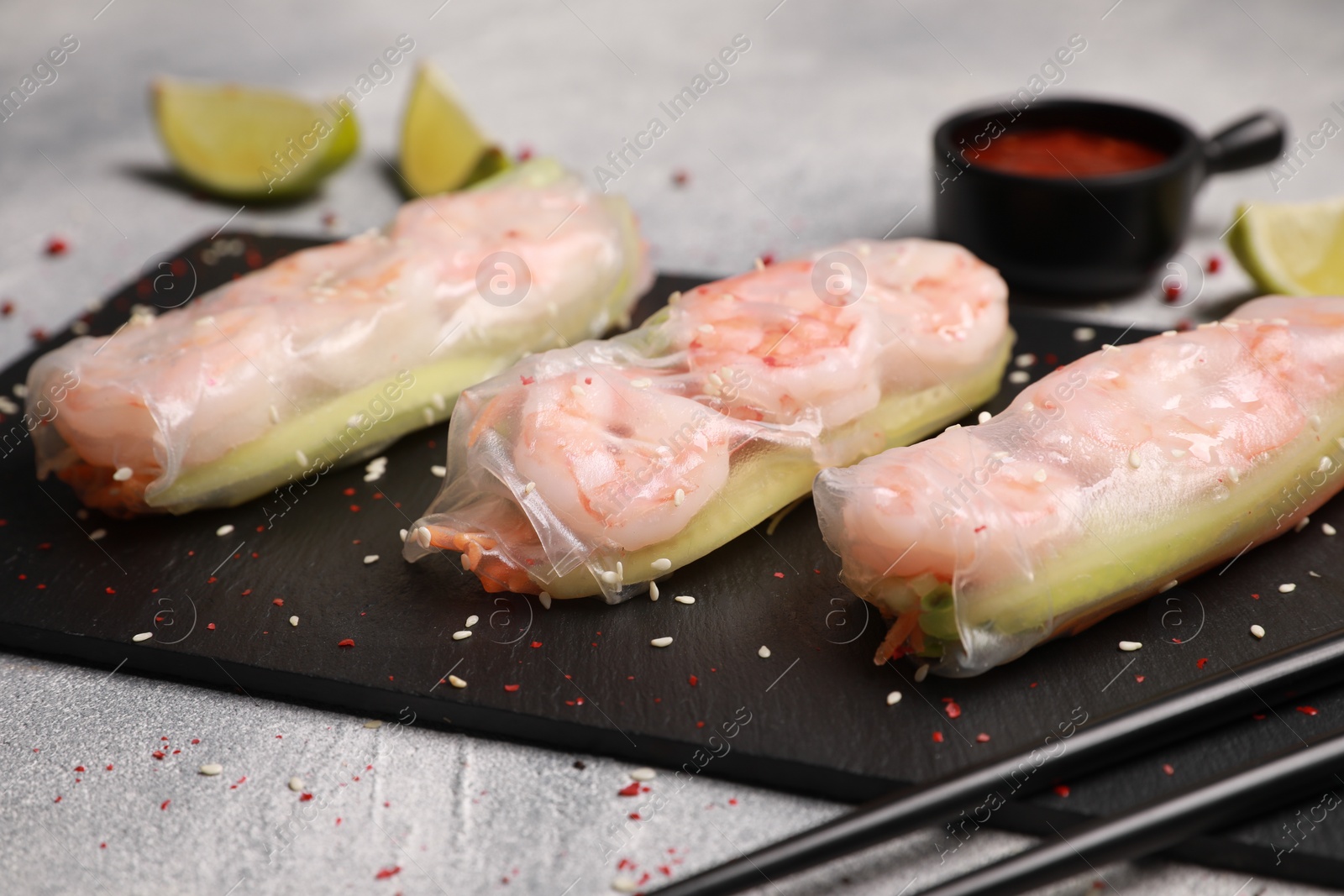 Photo of Slate plate with tasty spring rolls on grey textured table, closeup