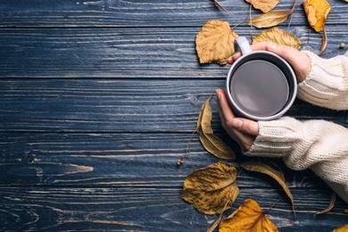 Woman with cup of hot drink at blue wooden table, top view with space for text. Cozy autumn atmosphere