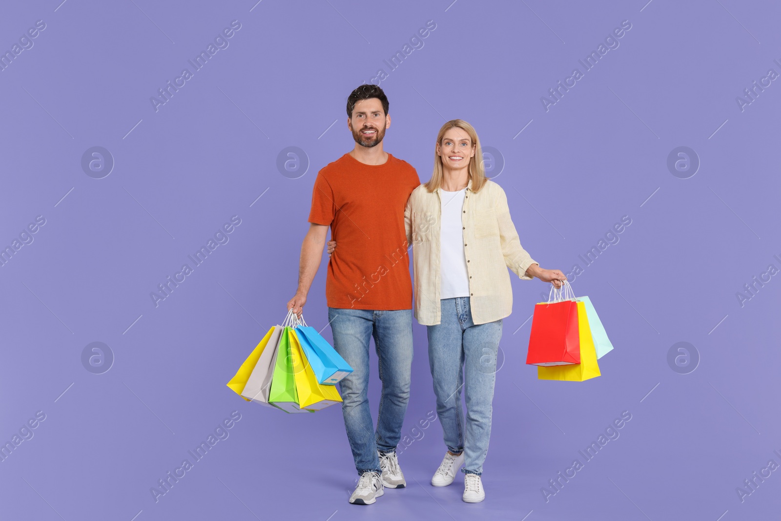 Photo of Family shopping. Happy couple with many colorful bags on violet background