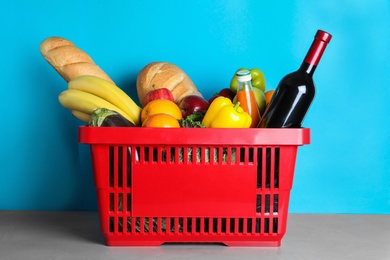 Shopping basket with grocery products on grey table against light blue background