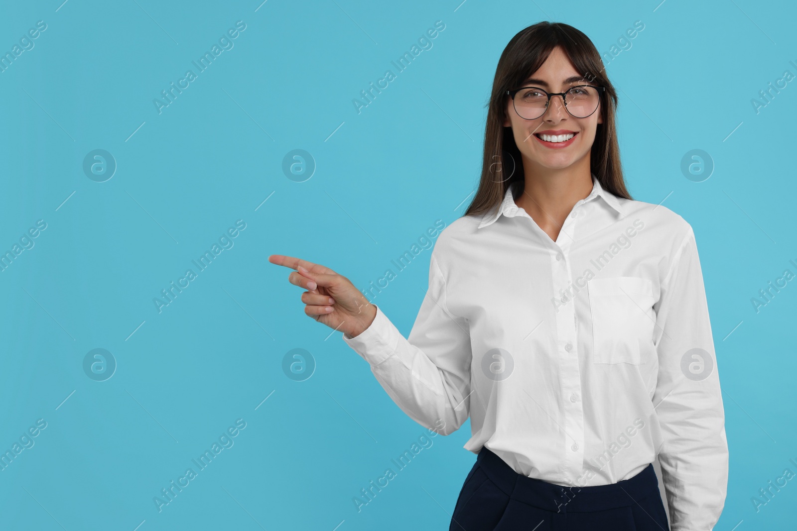 Photo of Portrait of happy secretary pointing at something on light blue background. Space for text