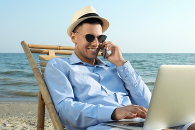 Photo of Happy man with laptop talking by mobile phone on beach. Business trip