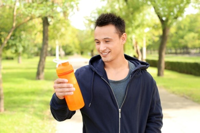 Man with bottle of protein shake in green park