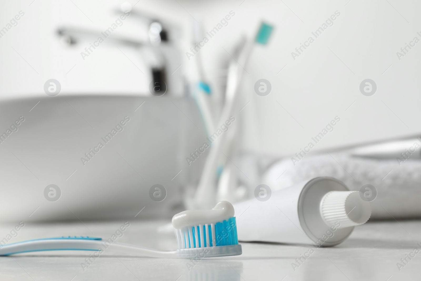Photo of Plastic toothbrush with paste and tube on white countertop in bathroom, closeup. Space for text