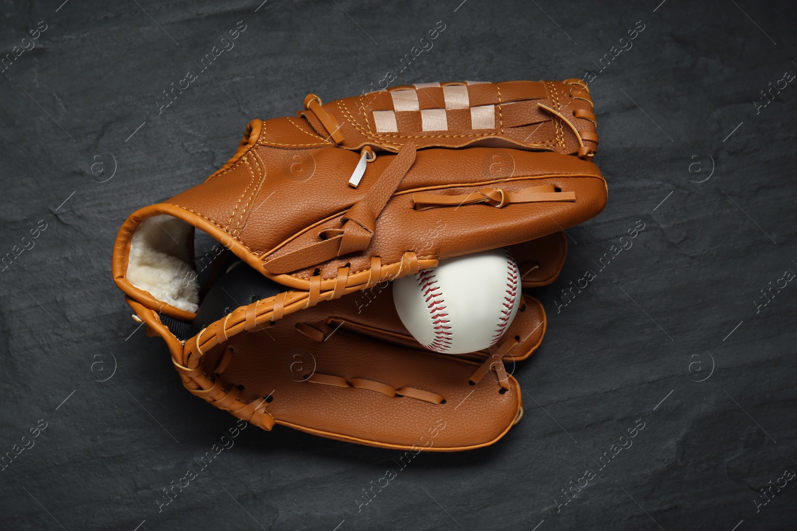 Photo of Catcher's mitt and baseball ball on black slate background, top view. Sports game