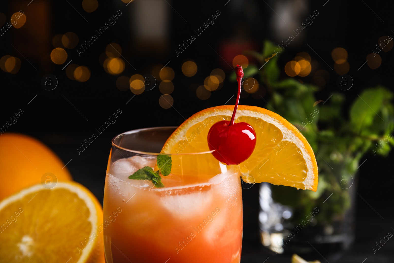 Photo of Fresh alcoholic Tequila Sunrise cocktail against festive lights, closeup