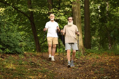 Photo of Two senior friends performing Nordic walking in forest. Low angle view