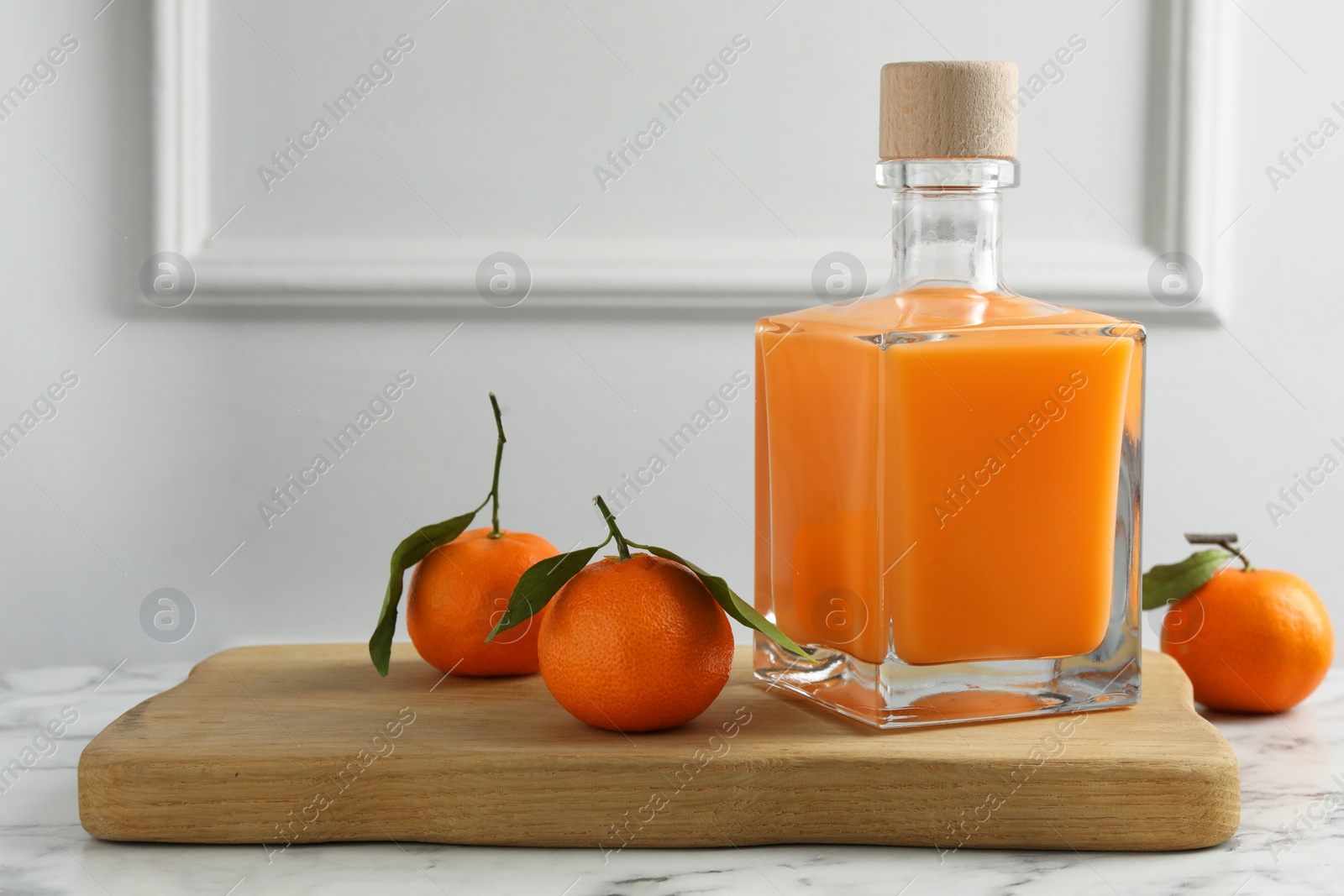 Photo of Delicious tangerine liqueur in bottle and fresh fruits on white marble table, space for text