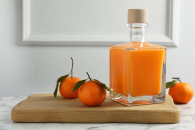 Delicious tangerine liqueur in bottle and fresh fruits on white marble table, space for text