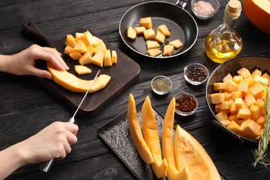 Photo of Woman cutting fresh pumpkin at black wooden table, closeup