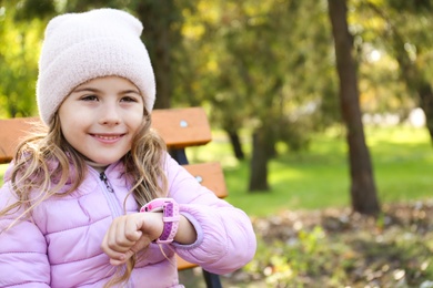 Photo of Little girl with stylish smart watch on bench outdoors