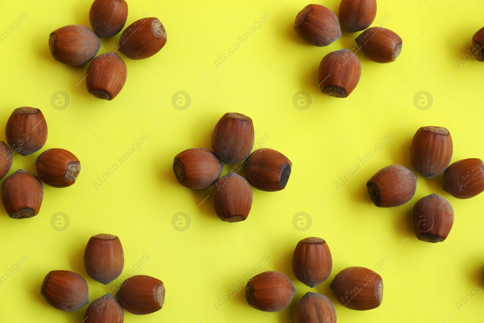 Photo of Pattern of hazelnuts on yellow background, flat lay