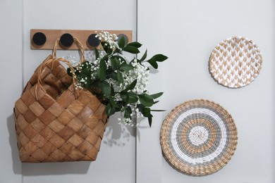 Stylish wicker basket with bouquet of flowers hanging on wooden rack indoors