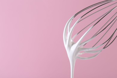 Whisk with whipped cream on pink background, closeup. Space for text