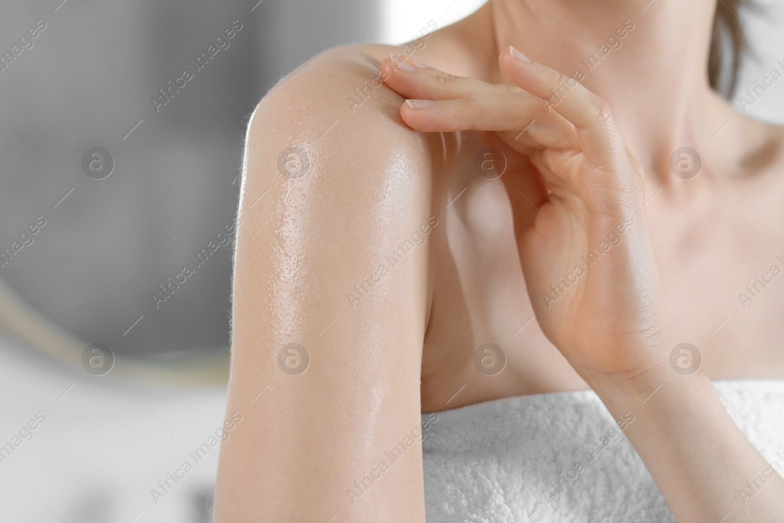 Photo of Woman applying body oil onto shoulder in bathroom, closeup